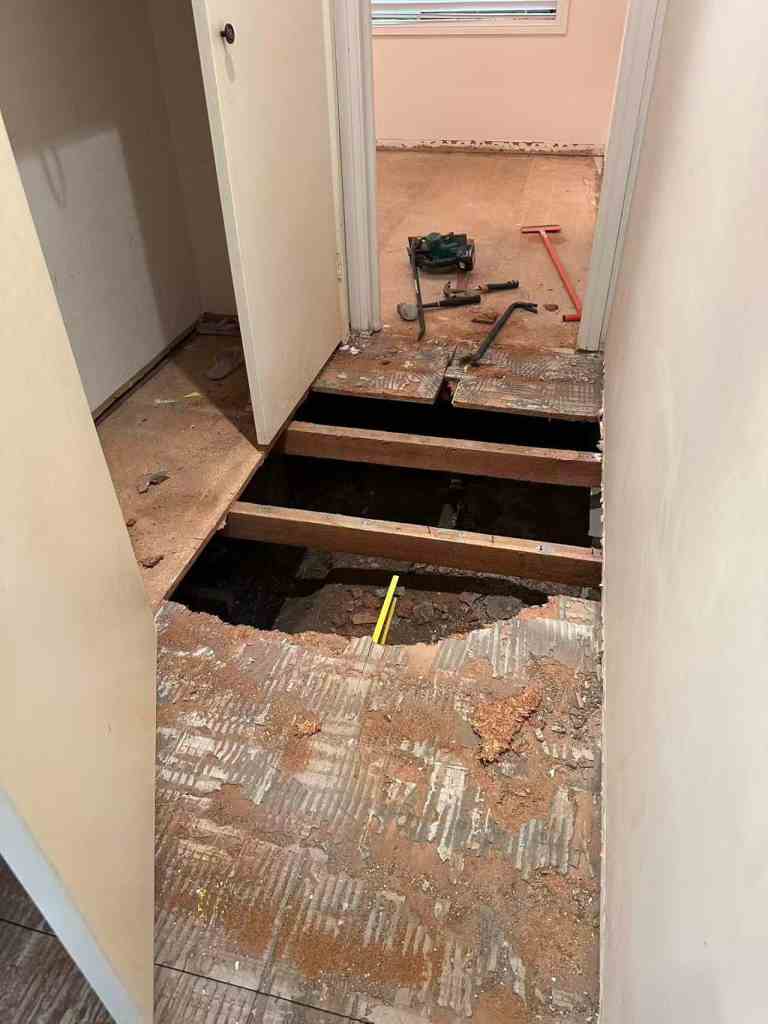 Shows exposed floor joists and construction tools in a hallway.