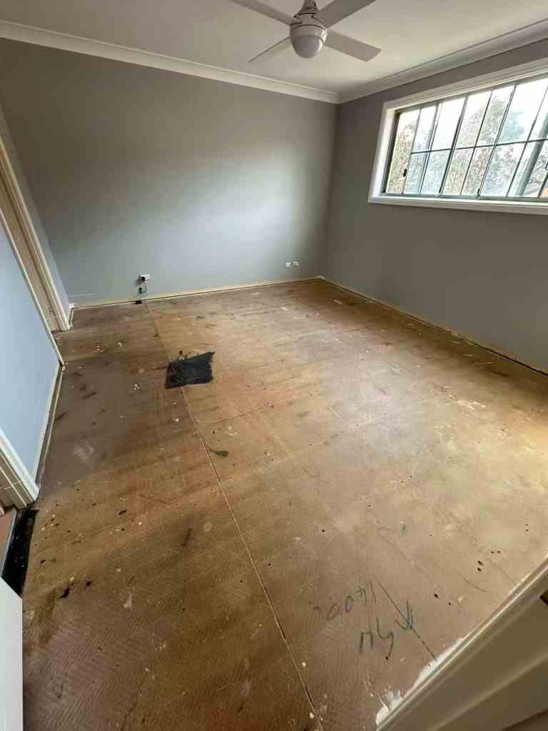Bright empty room with large window, bare floor, and ceiling fan.