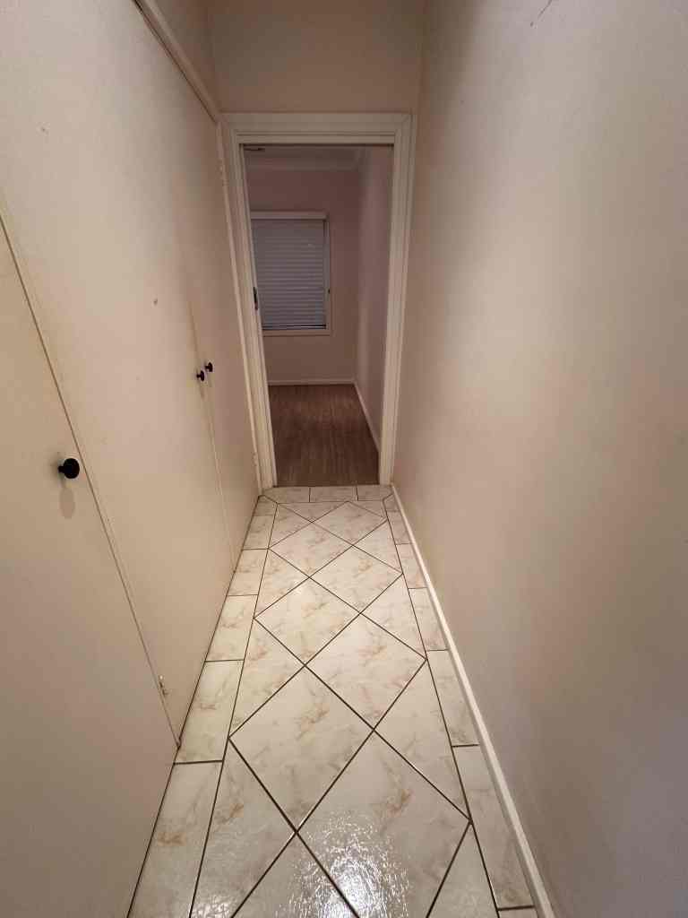 Long narrow hallway with tiled floor and white walls.